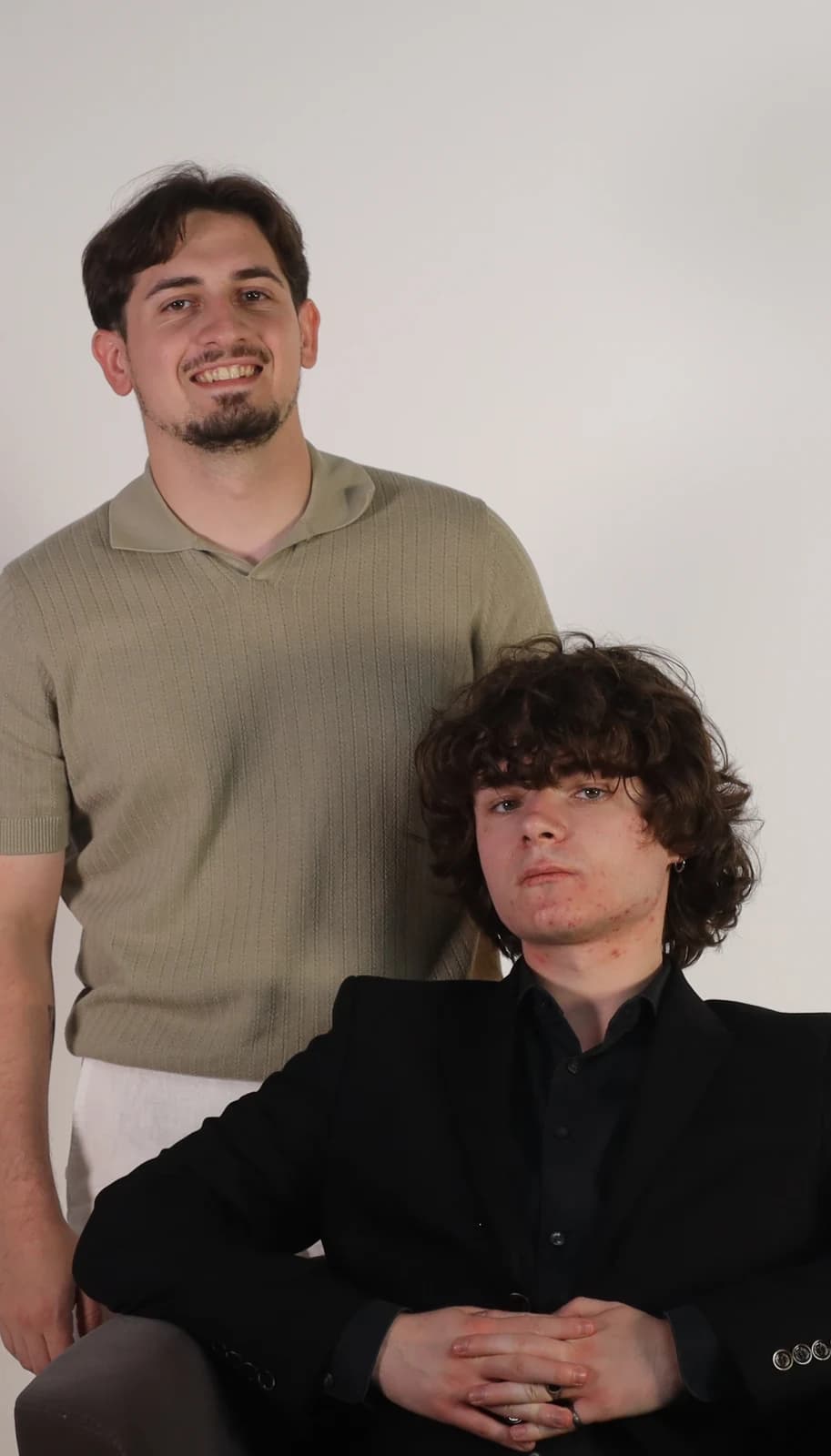 The two GENSAI founders — one standing in a knit polo, one seated in a dark blazer